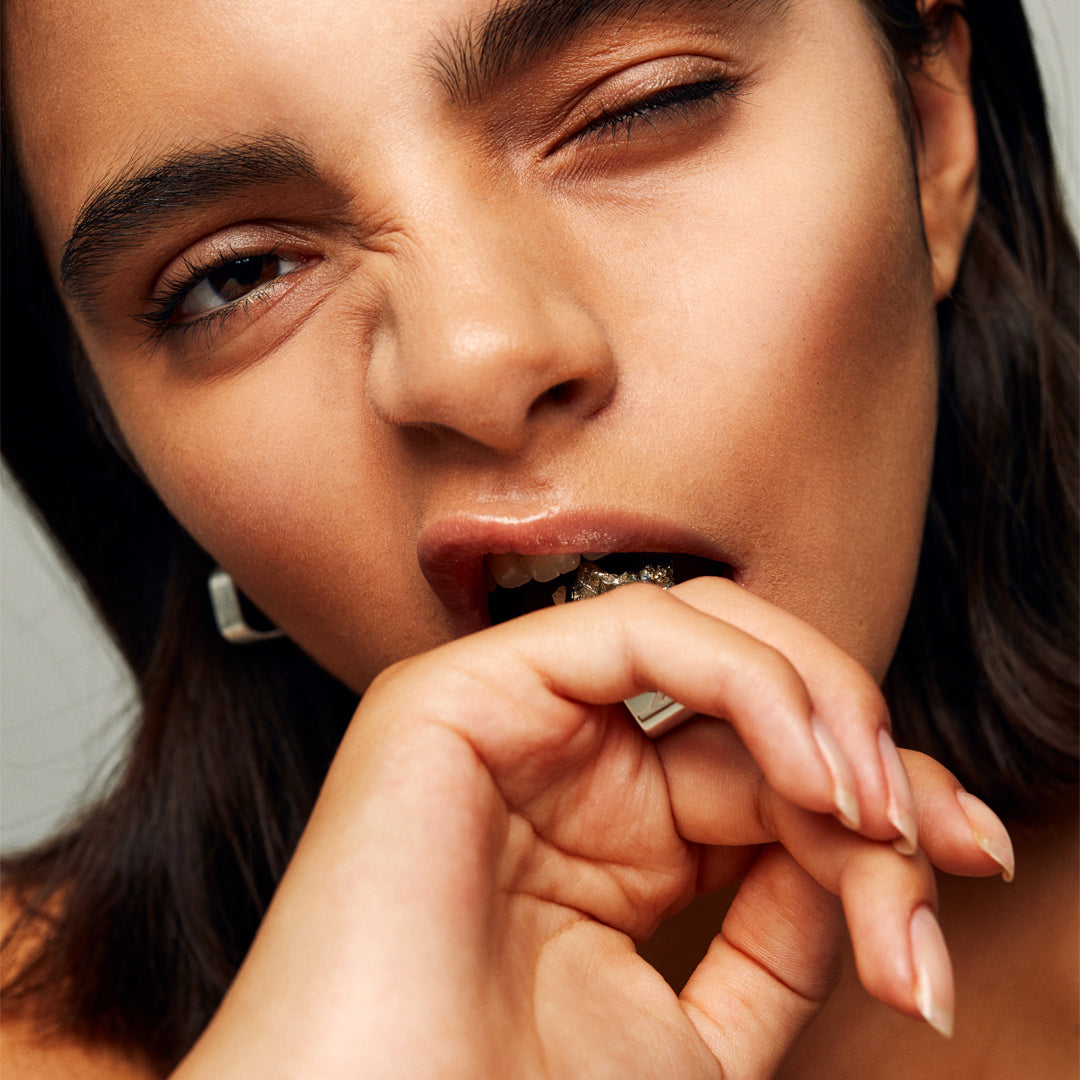 Model biting finger while wearing Roxx Pyrite Cube Ring by Märta Larsson. Raw pyrite ring styled with silver hoop earring — expressive and fashion-forward composition.