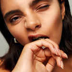 Model biting finger while wearing Roxx Pyrite Cube Ring by Märta Larsson. Raw pyrite ring styled with silver hoop earring — expressive and fashion-forward composition.