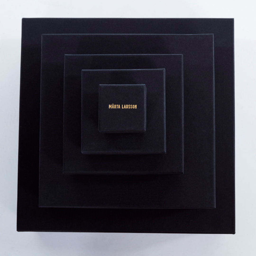 Roxx Pyrite Double Cube Ring by Märta Larsson placed in concentric black boxes with gold branding. Elegant packaging for handcrafted gemstone rings and luxury accessories.
