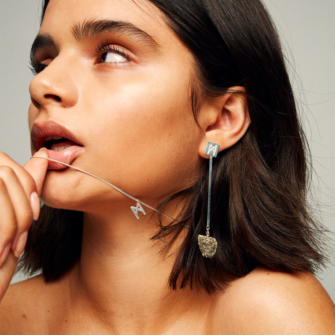 Model wearing Signature Necklace Polished Silver by Märta Larsson with the chain held in her mouth, a bold minimalist silver M-pendant look.