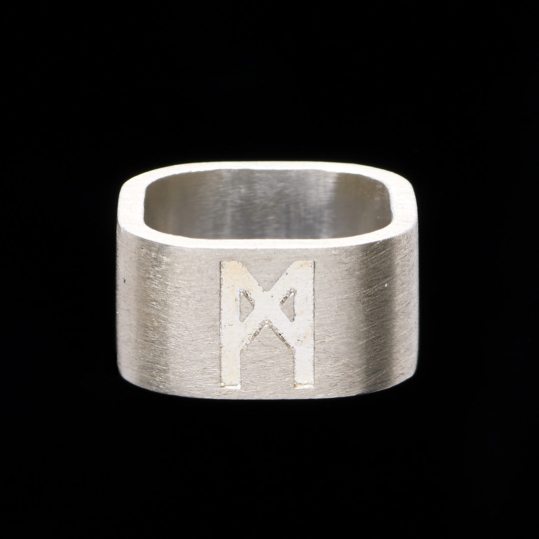 Brushed silver logo ring by Märta Larsson photographed against black background, emphasizing matte texture and engraved detail.