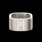 Brushed silver logo ring by Märta Larsson photographed against black background, emphasizing matte texture and engraved detail.