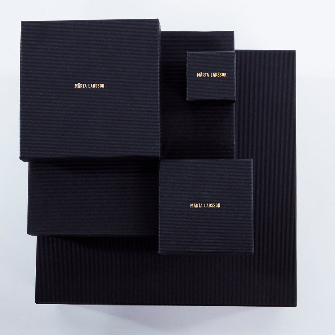 Assorted Märta Larsson jewelry boxes with branded logo, elegant packaging for designer crystal rings and luxury gemstone accessories.