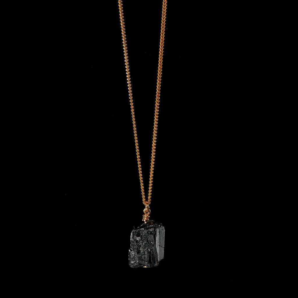 The Raw One Black Tourmaline Necklace by Märta Larsson with a raw crystal pendant on a gold-vermeil chain, a handcrafted piece with natural ridges and bold texture.