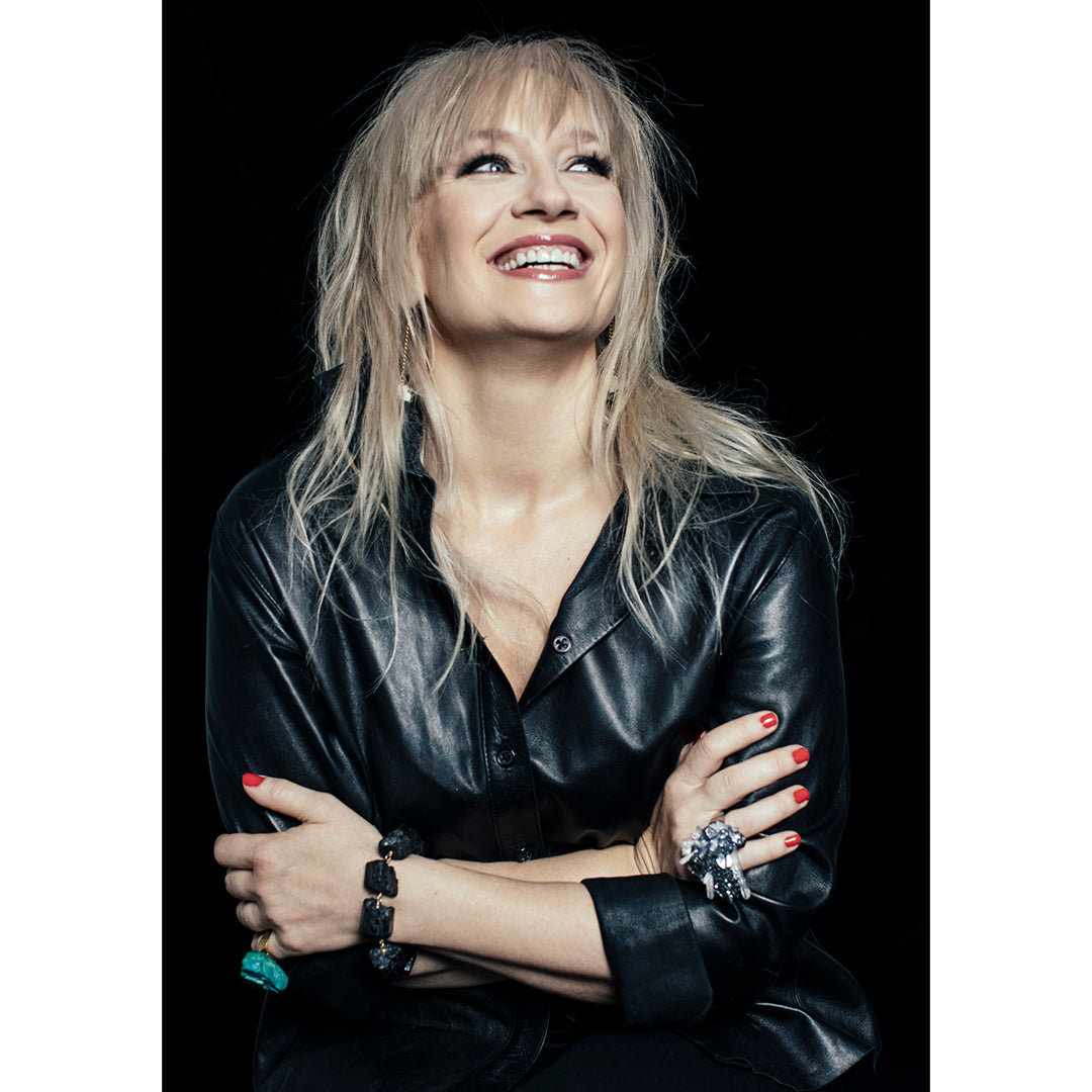 Model smiling in a black outfit wearing the Art Ring Special Edition Quartz by Märta Larsson, a clear quartz piece styled with red nails and layered bracelets.