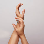 Two hands against a grey background, the upper hand wearing the Billie Ring Recycled Silver by Märta Larsson with raw stone texture and sculptural minimalist elegance.