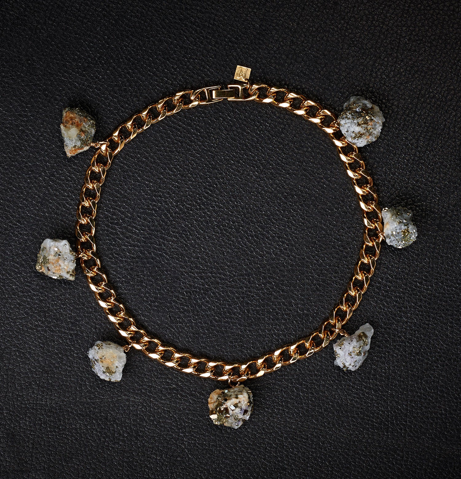 Collar Calcite Pyrite Necklace by Märta Larsson laid out on a black surface, featuring raw calcite-pyrite stones on a gold collar chain.