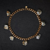 Collar Calcite Pyrite Necklace by Märta Larsson laid out on a black surface, featuring raw calcite-pyrite stones on a gold collar chain.