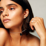 Close-up of a brown-haired model holding her necklace, wearing the MMM Brushed Silver Ring by Märta Larsson in brushed recycled silver with bold 10 mm engraved “M” logo band.