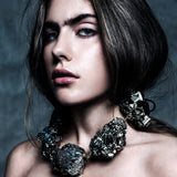 Model wearing the Not a Pearl Necklace XXL Art Edition Pyrite Crystal by Märta Larsson with voluminous hair and a textured backdrop, styled for confident artistic elegance.