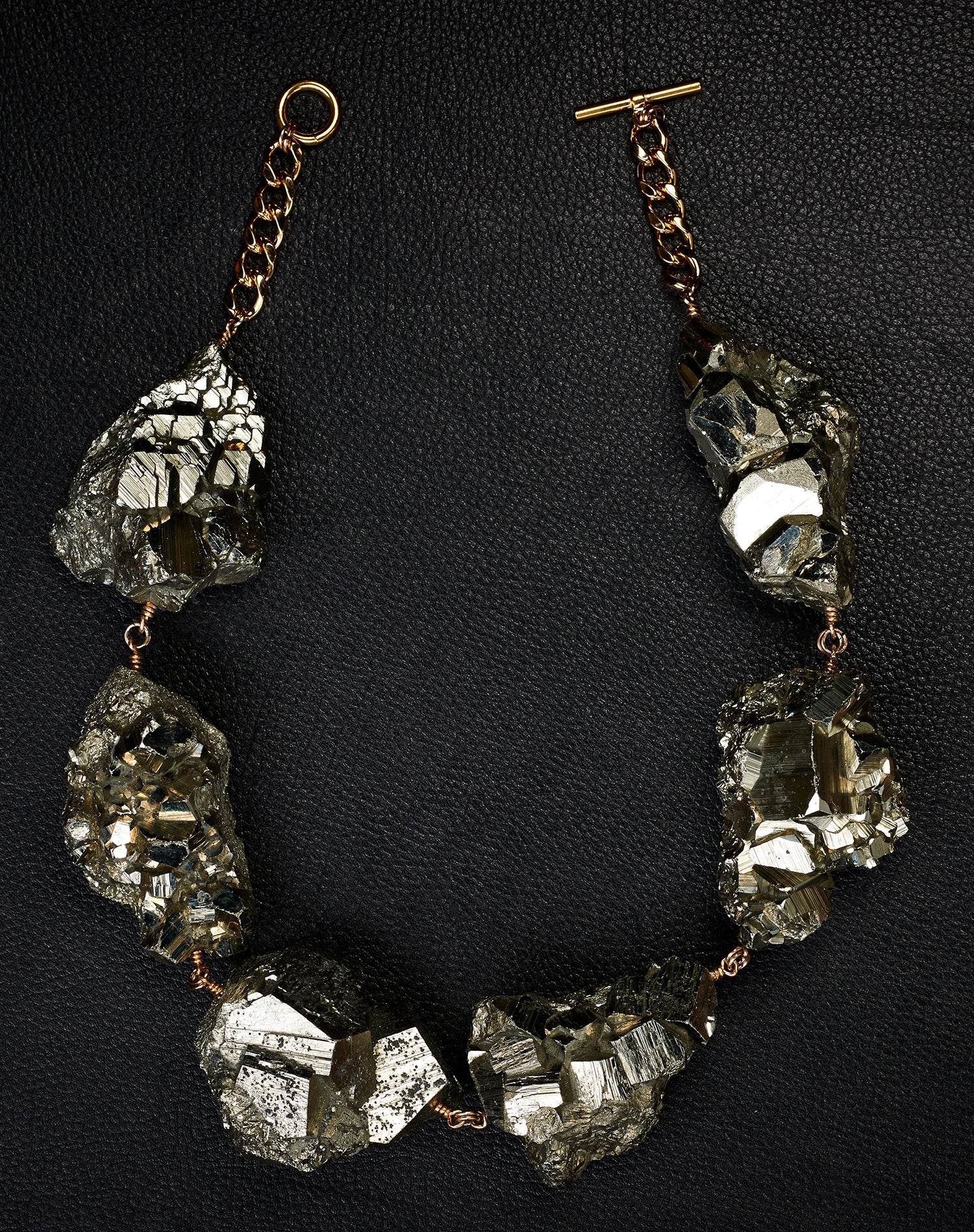 Not a Pearl Necklace XXL Art Edition Pyrite Crystal by Märta Larsson laid out on a black textured surface, featuring raw pyrite crystals on a gold chain.