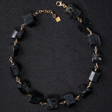 Not a Pearl Necklace Black Tourmaline by Märta Larsson laid out on a black textured surface, featuring raw black tourmaline stones on a gold chain.