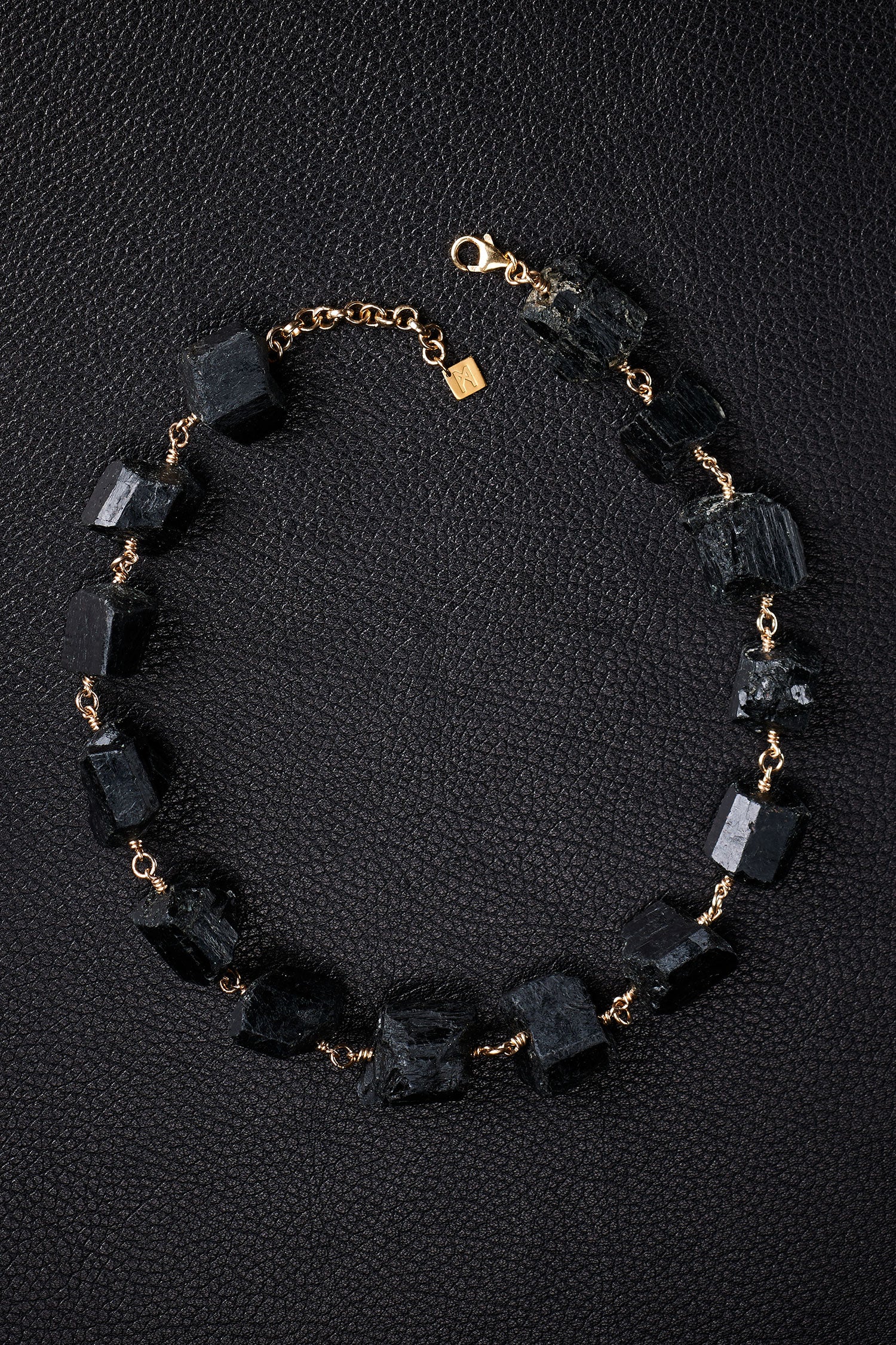 Not a Pearl Necklace Black Tourmaline by Märta Larsson laid out on a black textured surface, featuring raw black tourmaline stones on a gold chain.