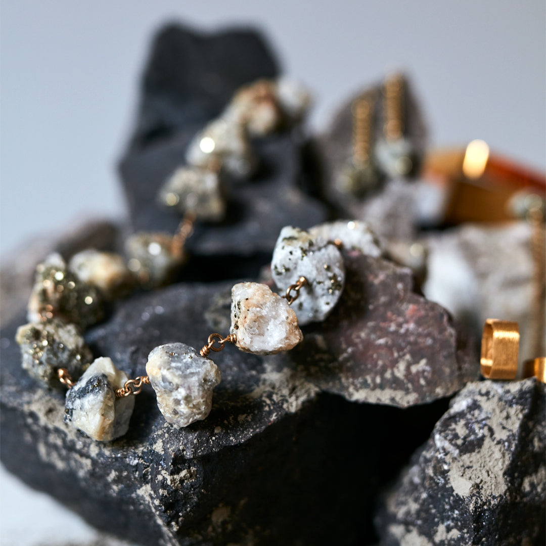 Not a Pearl Necklace Calcite Pyrite by Märta Larsson styled on rugged rocks, featuring raw crystal stones with a gold chain for natural strength.