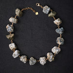 Not a Pearl Necklace Calcite Pyrite by Märta Larsson laid out on a black textured surface, featuring raw calcite-pyrite stones on a gold chain.