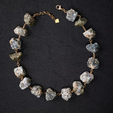 Not a Pearl Necklace Calcite Pyrite by Märta Larsson laid out on a black textured surface, featuring raw calcite-pyrite stones on a gold chain.