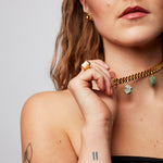 Model holding a necklace while wearing the bold, raw and sophisticated Märta Larsson Power Ring, a handcrafted rugged-stone gold-vermeil piece on the ring finger.