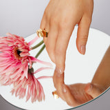 Hand reaching above a mirror beside a flower wearing the bold, raw and sophisticated Märta Larsson Power Ring, a nature-inspired gemstone statement piece on the ring finger.