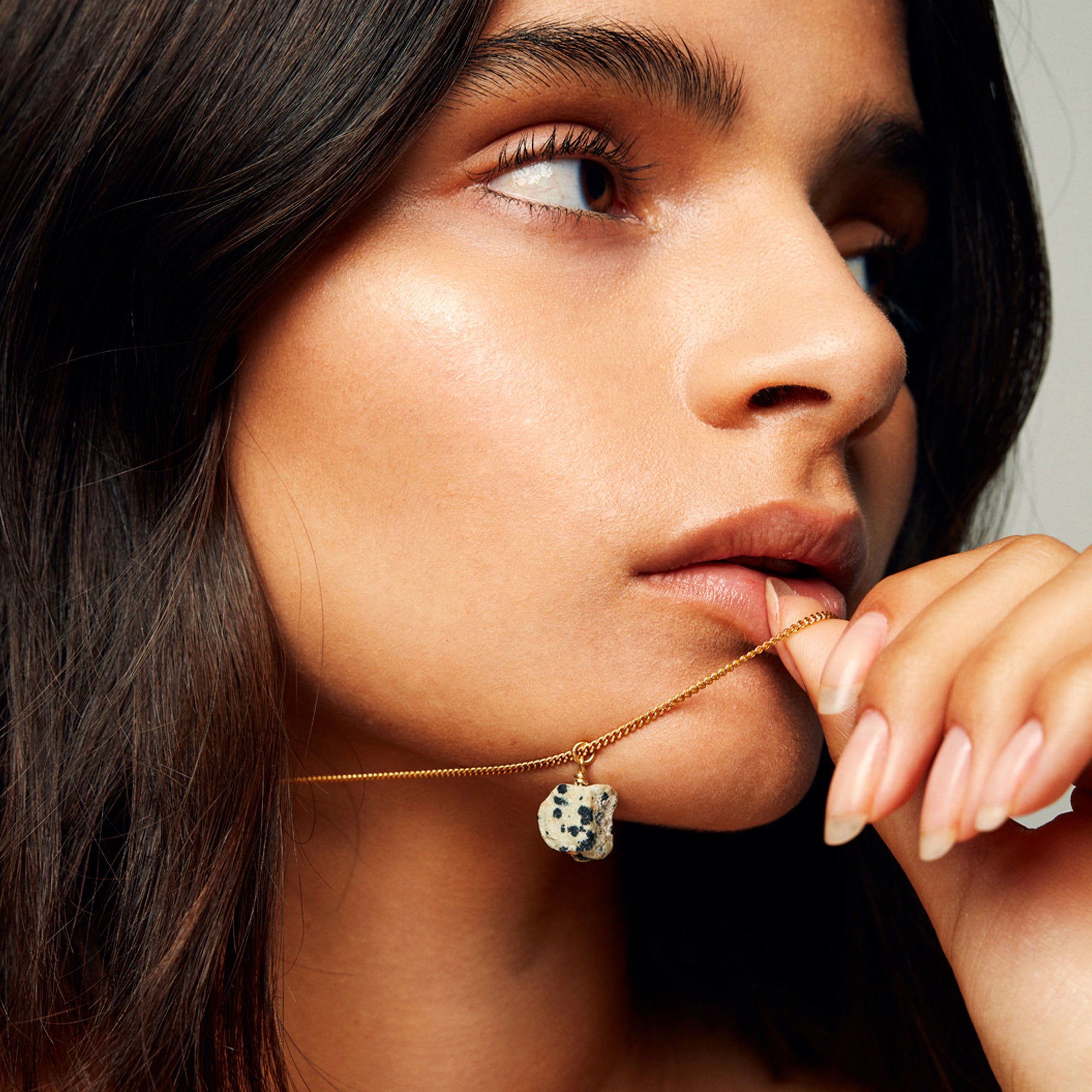 Model holding The Raw One Dalmatian Necklace by Märta Larsson with bear-shaped pendant, a playful raw dalmatian stone piece on gold vermeil chain.