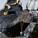 The Raw One Dalmatian Necklace by Märta Larsson displayed on volcanic rocks, a raw speckled stone pendant styled with gold jewelry.