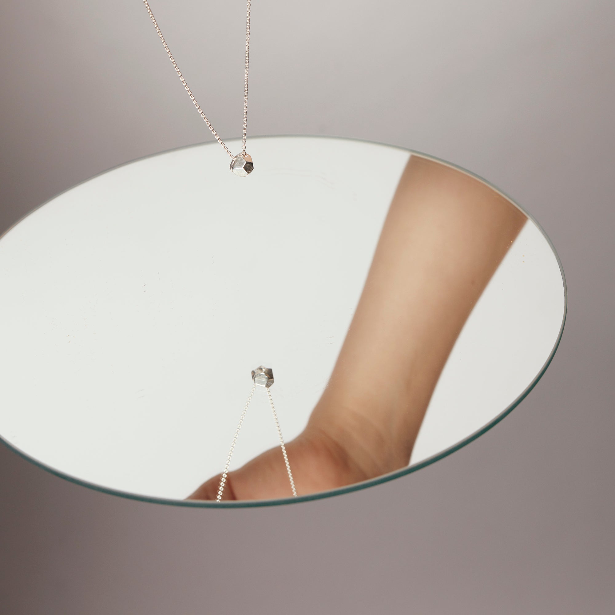 Rolling Stone Necklace by Märta Larsson reflected in a mirror, a recycled silver piece with a small geometric sculptural pendant.