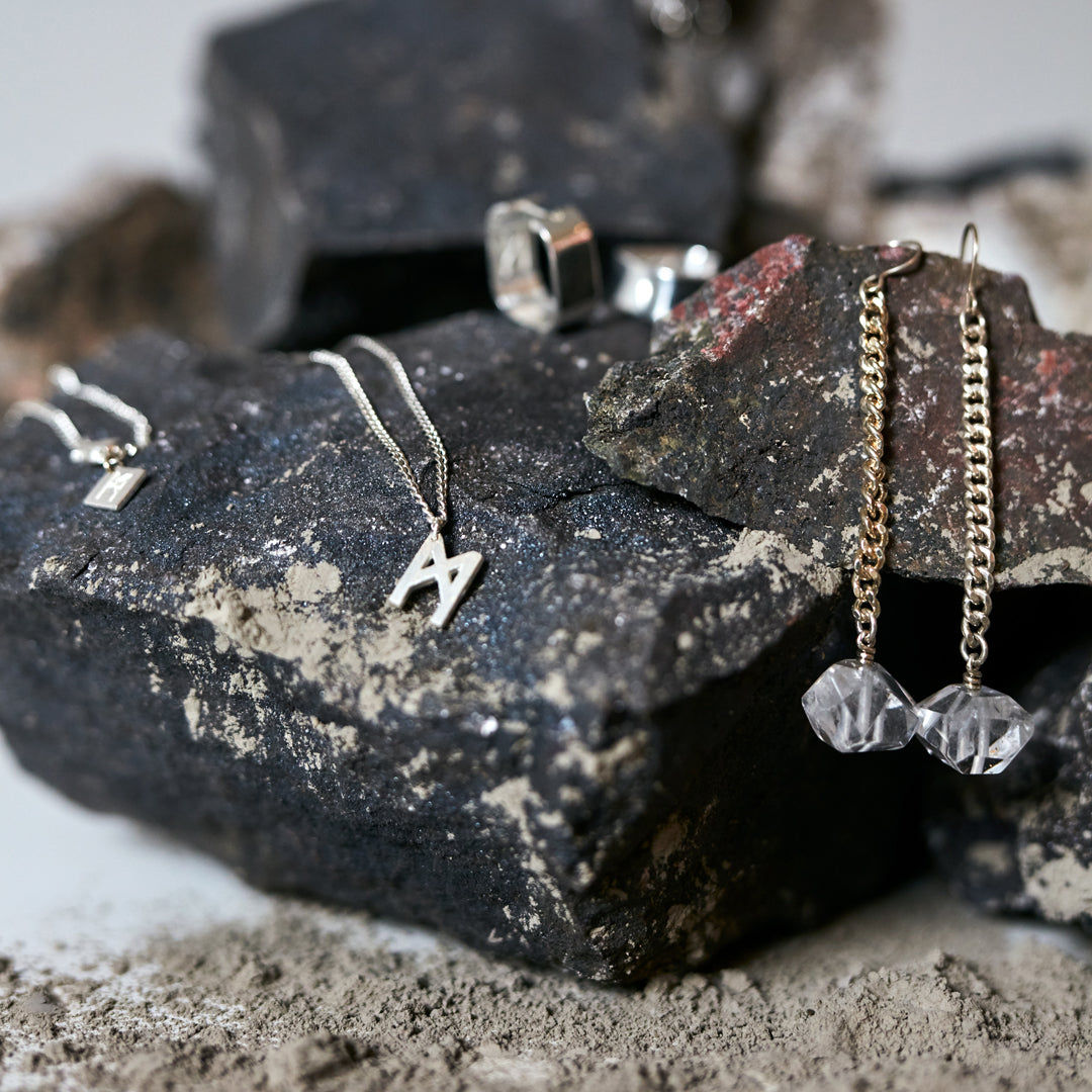 Jewelry styled on textured rocks featuring Signature Necklace Brushed Silver by Märta Larsson, a minimalist brushed-silver M charm necklace.