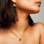 Model wearing the Signature Necklace in polished gold vermeil by Märta Larsson, an M-charm pendant styled with short hair and gold earrings.