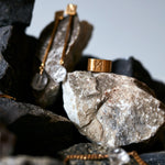 Signature Brushed Gold Ring by Märta Larsson placed on a stone among black, white, and grey stones, showcasing its 10 mm brushed 24 carat gold vermeil band with bold minimalist contrast.