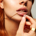 Model holding The Raw One Rose Quartz Necklace by Märta Larsson near lips, featuring a raw rose quartz pendant on a gold chain.